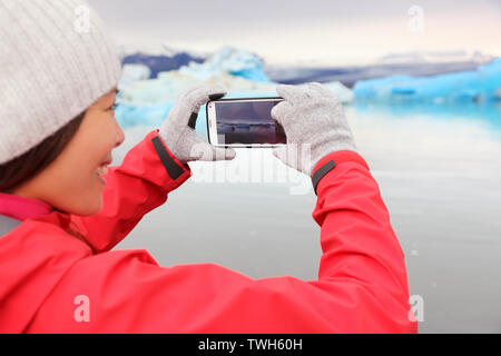 Woman taking photo smartphone par Jokulsarlon glacial lagoon / lac glaciaire sur l'Islande. Professionnels tourisme billet à l'aide de smart téléphone appareil avec sa nature paysage islandais avec Vatnajokull. Banque D'Images
