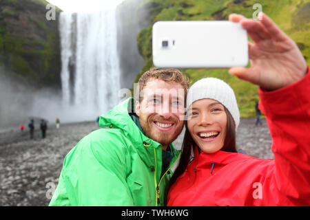 Couple selfies smartphone prendre photo de cascade en plein air en face de Skogafoss sur l'Islande. Visite de deux célèbres attractions touristiques et monuments de la nature islandaise paysage sur Golden Circle. Banque D'Images