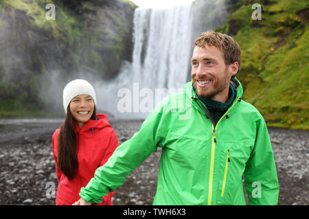 Heureux couple holding hands en cascade à l'extérieur en face de Skogafoss sur l'Islande. Visite de deux célèbres attractions touristiques et monuments de la nature islandaise paysage sur Golden Circle. Banque D'Images