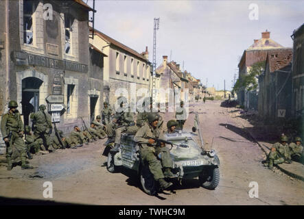 Parachutistes américains en jeep allemande patrouillant Carentan tandis que d'autres soldats américains reste contre un bâtiment, Normandie, France, juin 1944 Banque D'Images