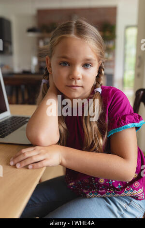 Cute girl looking at camera, assis sur une table à manger dans une maison confortable Banque D'Images