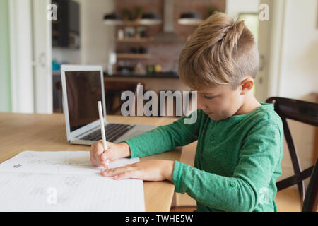 Cute boy doing homework at table à manger dans une maison confortable Banque D'Images