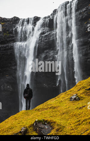 Lonely wanderer / randonneur debout en face de Fossa, la plus grande chute d'eau sur les îles Féroé, comme vu au début du printemps (îles Féroé, Danemark) Banque D'Images