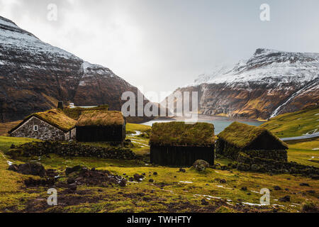 Féroïen typiques cabines recouvertes d'herbe dans le petit village Saksun, au début du printemps avec ses montagnes couvertes de neige et de mer bleu foncé (îles Féroé) Banque D'Images