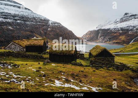 Féroïen typiques cabines recouvertes d'herbe dans le petit village Saksun, au début du printemps avec ses montagnes couvertes de neige et de mer bleu foncé (îles Féroé) Banque D'Images