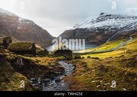 Féroïen typiques cabines recouvertes d'herbe dans le petit village Saksun, au début du printemps avec ses montagnes couvertes de neige et une petite rivière (îles Féroé) Banque D'Images