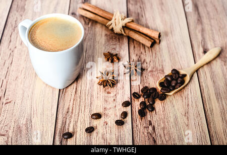 Tasse de café chaud, des bâtons de cannelle et les grains de café s'échappant d'un scoop en bois rustique en bois sur table. Close-up. Banque D'Images