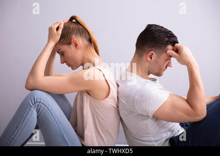 Triste jeune couple assis dos à dos sur le plancher à la maison Banque D'Images