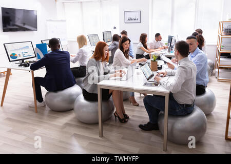 Groupe de Multi-ethnic Woman Sitting on Fitness Ball avoir discuter tout en travaillant à l'Office de Tourisme Banque D'Images