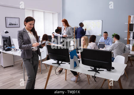 Certain Young Businesswoman Holding Document en face de ses collègues au bureau Banque D'Images