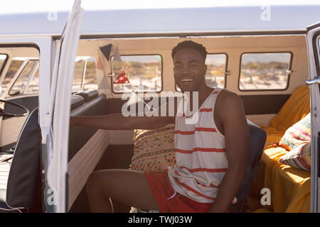 Jeune homme assis dans le camping-car at beach Banque D'Images
