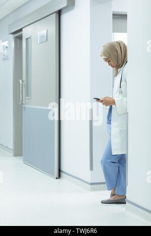 Femme médecin en hijab à l'aide de téléphone mobile à couloir Banque D'Images