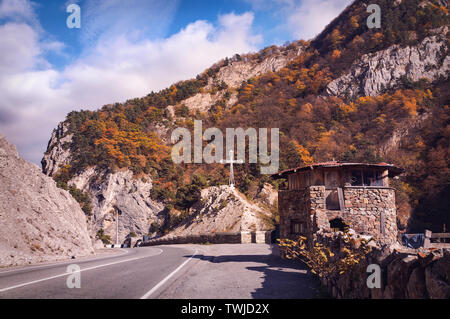 Vue du Caucase - une croix chrétienne à côté d'une route étroite entre les montagnes de l'automne brunâtre plus grande chaîne de montagnes du Caucase, en Ossétie du Nord Banque D'Images