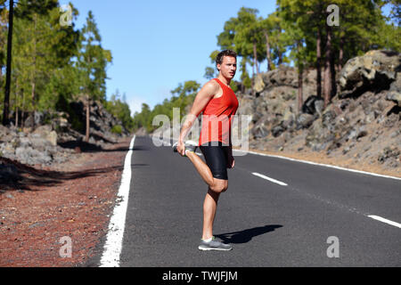 Runner man stretching cuisse et jambes suite à l'utilisation sur route forestière en montagne. Beau caucasien homme modèle de remise en forme en plein air. Banque D'Images