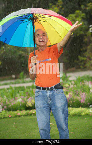 Old man standing under an umbrella and smiling Stock Photo