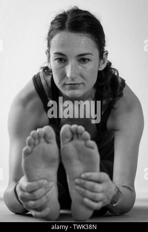 Portrait noir et blanc vue rapprochée d'une femme brune du milieu de la trentaine se plie en Paschimottanasana, assis vers l'avant la posture de yoga plie fermement les pieds Banque D'Images