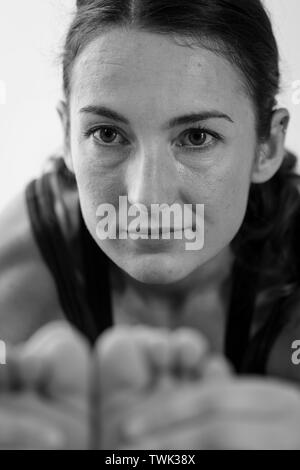 Portrait noir et blanc vue rapprochée d'une femme brune du milieu de la trentaine se plie en Paschimottanasana, assis vers l'avant la posture de yoga plie fermement les pieds Banque D'Images