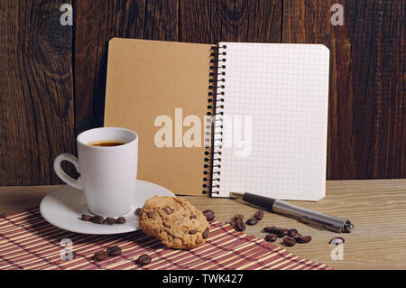 Ouvrir le bloc-notes et tasse de café avec des biscuits au chocolat sur la vieille table en bois Banque D'Images
