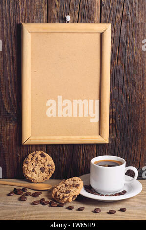 Tasse de café chaud avec des cookies au chocolat et cadre vide sur le mur en bois Banque D'Images