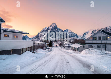 Maison couverte de neige avec road entouré de la montagne, au coucher du soleil, Reine village, îles Lofoten, Norvège Banque D'Images
