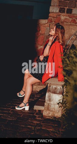 Jolie jeune femme en robe et veste rouge sur fond urbain rue de la ville. Vieille ville. Photo verticale Banque D'Images