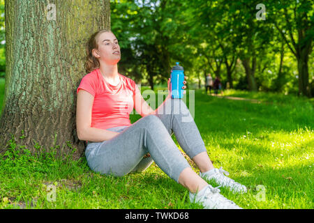 Une jeune femme prend une pause dans le sport et est assis sous un arbre Banque D'Images