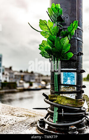 Carte de prière religieuse liée à un poteau de métal avec des branches avec des feuilles de plastique vert sur un pont, un lieu du souvenir, jour de pluie en Irlande Banque D'Images