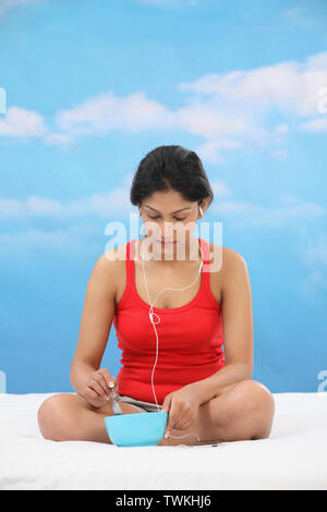 Femme assise sur le lit et de manger un bol de Banque D'Images