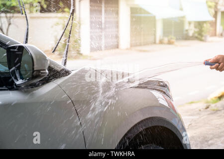 Lavage manuel voiture avec de l'eau pression flexible sur voiture blanche Banque D'Images