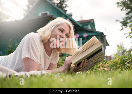 European blonde mature femme lisant un livre dans le jardin. Banque D'Images