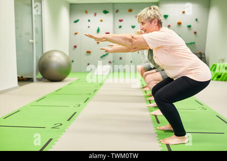 Groupe des aînés vital de faire des squats dans la classe de conditionnement physique pour la force et de l'équilibre Banque D'Images