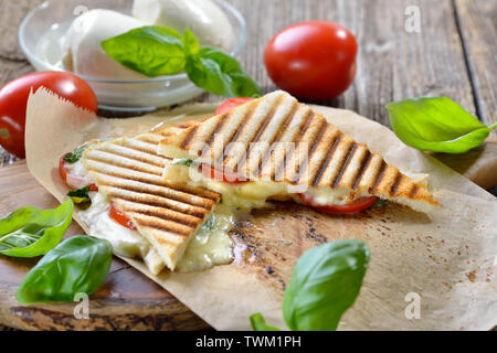 Panini grillé et pressé à caprese tomate, mozzarella et basilic, servi sur du papier sandwich sur une table en bois Banque D'Images