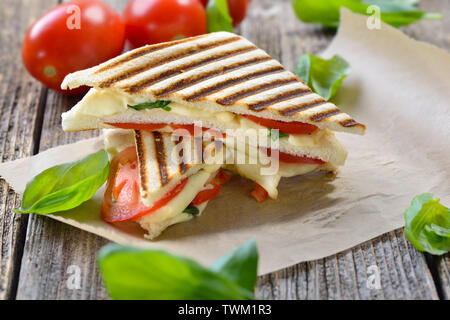 Panini grillé et pressé à caprese tomate, mozzarella et basilic, servi sur du papier sandwich sur une table en bois Banque D'Images