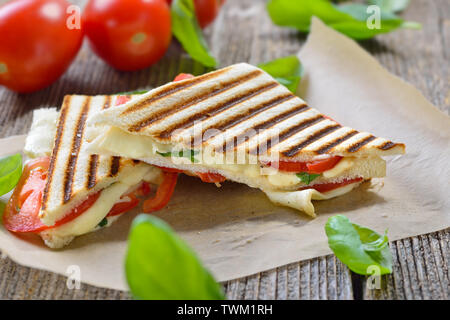 Panini grillé et pressé à caprese tomate, mozzarella et basilic, servi sur du papier sandwich sur une table en bois Banque D'Images