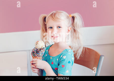 Funny Cute adorable preschool girl blonde caucasien enfant aux yeux bleus et pigtails eating holding large cornet gaufré avec la crème glacée et de paillettes. H Banque D'Images