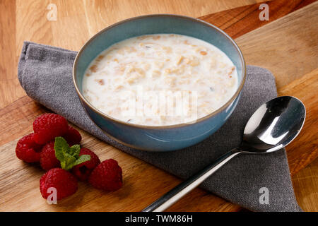 Délicieux bol de porridge et raspberrys tourné sur une planche en bois avec une serviette et des couverts. Banque D'Images