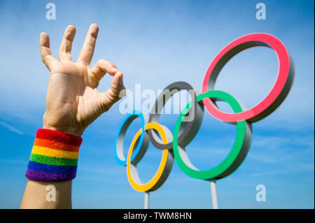 Londres - 4 mai 2019 : une main portant des gay pride rainbow bracelet de couleur fait un geste OK en face d'anneaux olympiques sous ciel bleu. Banque D'Images