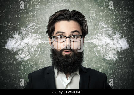 Homme barbu avec de la fumée sortir de ses oreilles, plus de tableau noir portant des formules et calculs scientifiques en physique et en mathématiques, conce Banque D'Images