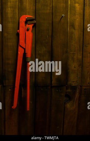 Ancienne clé à tuyau orange accroché sur le mur en bois Banque D'Images