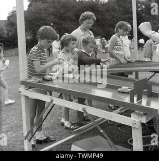 1967, historiques, des enfants dans un champ de jouer à un jeu avec des petites voitures à un décrochage à Gojomo fete, Buckinghamshire, Angleterre. Banque D'Images