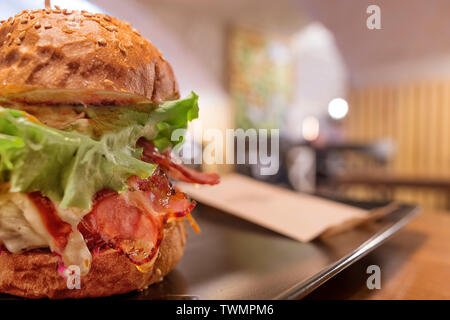 Big tasty burger avec du jambon et de la salade contre l'arrière-plan flou artistique cafe. Selective focus sur le burger Banque D'Images