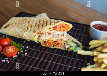 Shawarma et frites avec sauce se trouve sur un bambou foncé arrière-plan. L'Est de la restauration rapide. Belle photo avec le gros sel, tomates cerises, ciabatta Banque D'Images