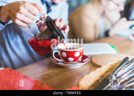 Berry plateau est versé dans une tasse de thé rouge rouge. avec des baies est versé dans un verre avec pois blancs et points. Fédération des plats à l'ancienne dans la restaura Banque D'Images