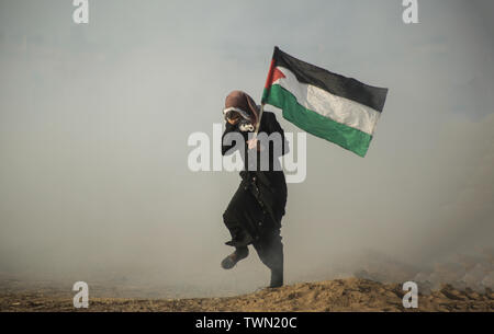 Un manifestant palestinien s'enfuit avec un drapeau de fumée de gaz lacrymogènes tirés sur eux pendant les affrontements.palestiniens se sont affrontés avec les forces israéliennes au cours d'une manifestation appelant à la levée du blocus israélien de Gaza et exigeante pour le droit de retourner dans leur patrie, à l'Israel-Gaza clôture frontalière dans le sud de la bande de Gaza. Banque D'Images