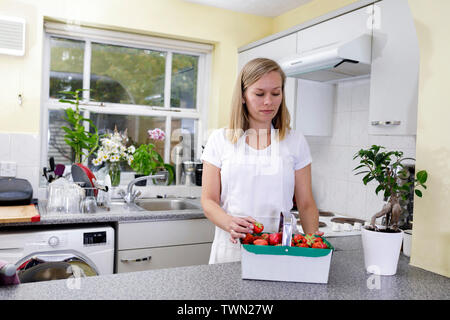 Une jeune femme tient un panier de fraises biologiques dans la cuisine. Les fraises fraîches sortant du jardin sont préparées par une femme de ménage sur un b Banque D'Images