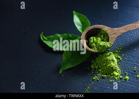 Thé Matcha en poudre dans les feuilles de thé avec une cuillère de bois sur un fond sombre avec copie espace Banque D'Images
