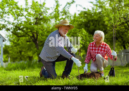 Femme souriante. Transmission d'appel femme en souriant tout en regardant son mari la plantation d'arbres Banque D'Images