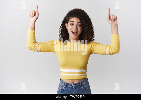 Impressionné animé cheerful young hispanic girl heureusement pointant vers le haut, soulevé l'index ravis des nouvelles excitantes dit joyeusement permanent white Banque D'Images