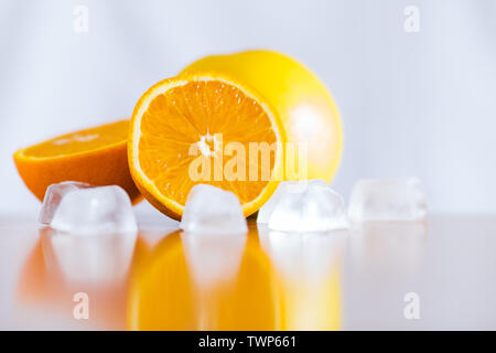 Les oranges fraîches et des cubes de glace réfléchissante sur table en bois Banque D'Images