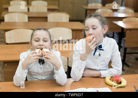 Les filles de l'adolescence de déjeuner à l'école classe. Une fille est végétarienne avec des fruits, un autre mange un sandwich avec du fromage et de la saucisse. Banque D'Images